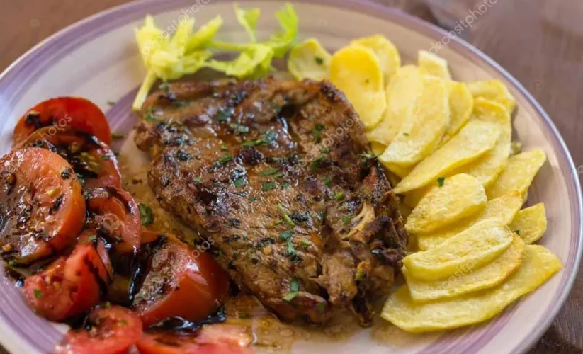 Bistecche di maiale con patate e pomodori al forno