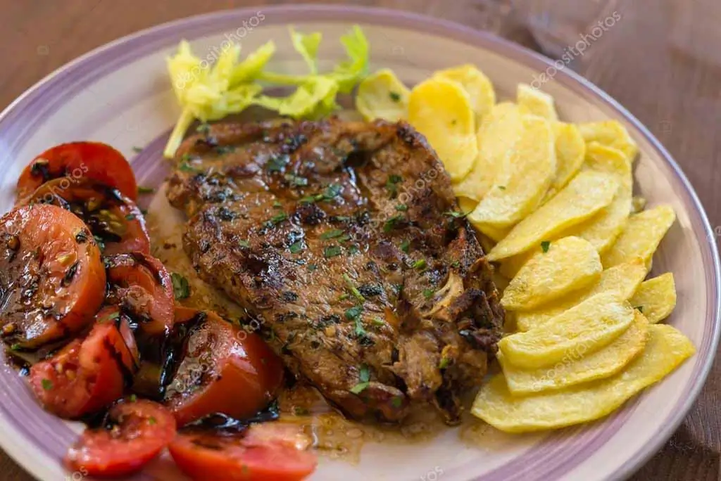 Bistecche di maiale con patate e pomodori al forno